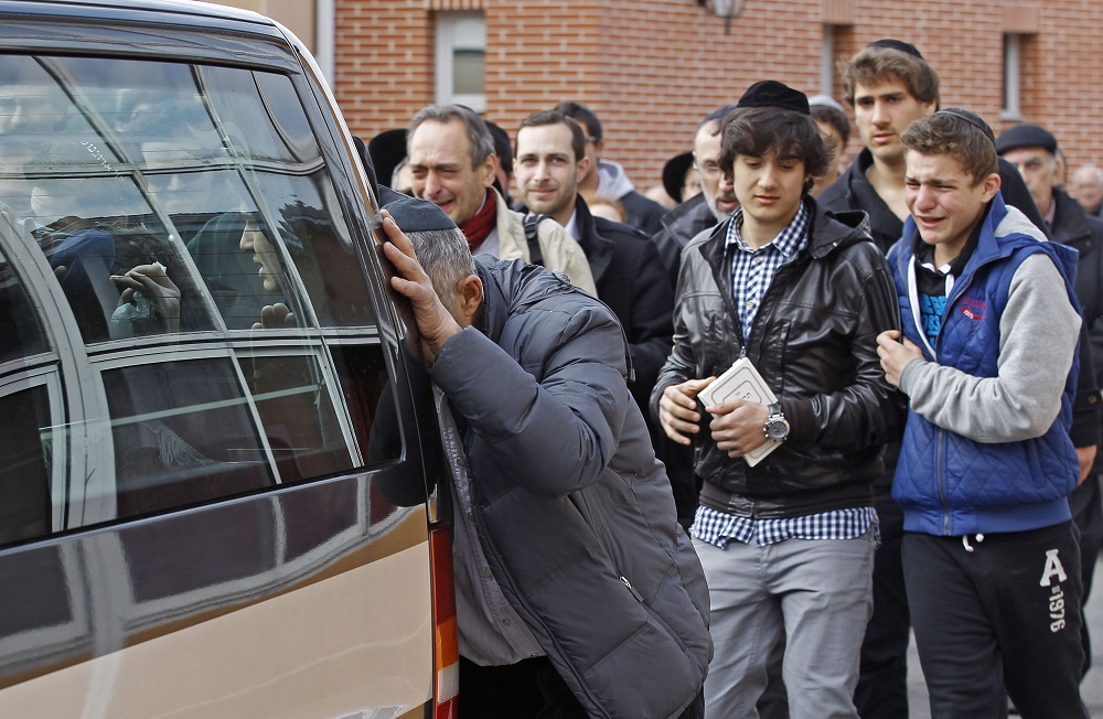 Toulouse, 2012. március 20. Az áldozatokat szállító furgont kísérik gyászolók, amint a jármû az Ozar Hatorah zsidó iskolából a toulouse-i repülõtérre indul egy nappal az után, hogy egy robogóval közlekedõ fegyveres lövöldözött az iskola elõtt és négy francia-izraeli állampolgárt megölt, kettõt súlyosan megsebesített. A halálos áldozatok között van egy apa és két fia. A holttesteket Izraelben temetik el. A hatóságok szerint a gyilkos azonos azzal a férfival, aki ebben a hónapban megölt három színes bõrû katonát a Toulouse közelében fekvõ Montaubanban. (MTI/AP/Remy de la Mauviniere)
