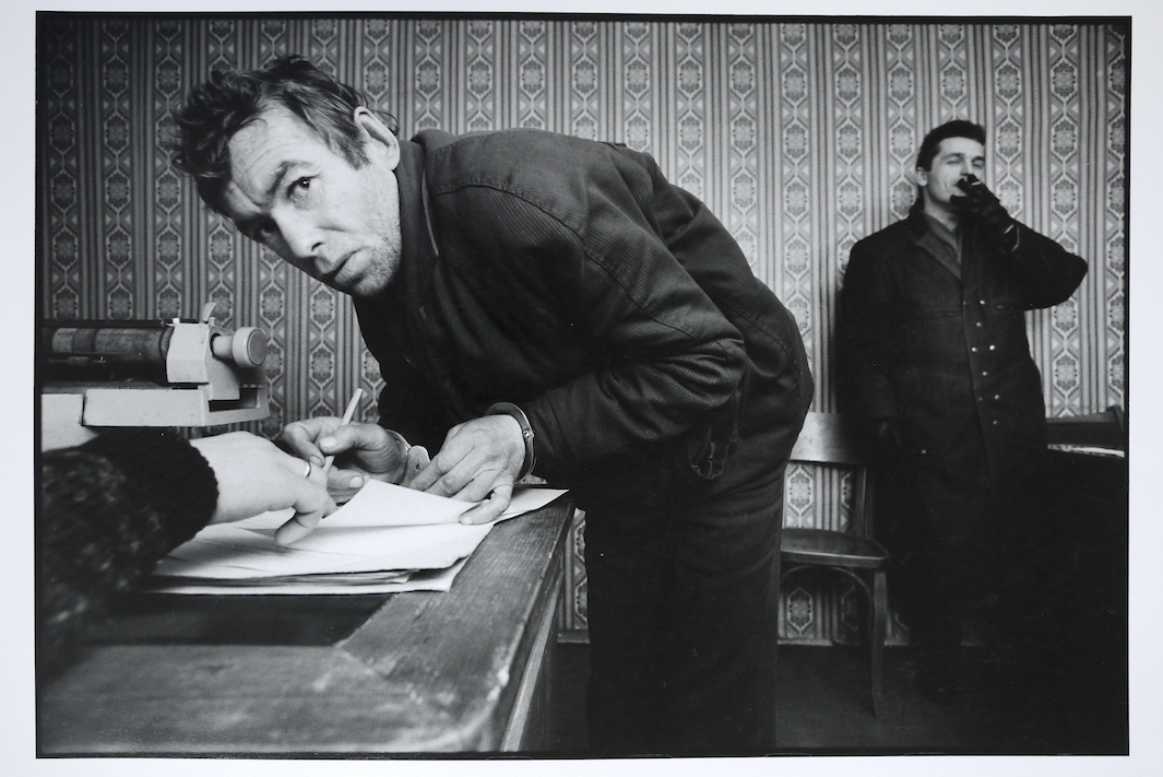Egy tolvaj tanúvallomását írja alá a helyi rendőrörsön, háttérben az őt őrizetbe vevő rendőrrel, 1992. december