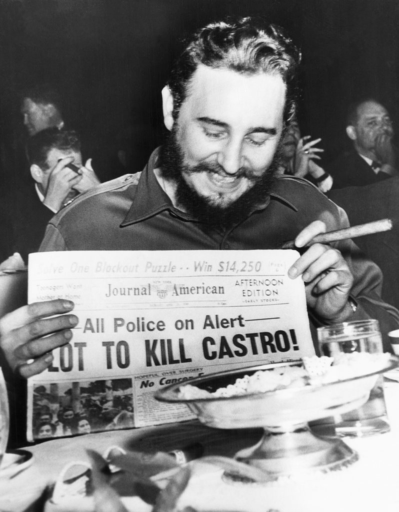 (Original Caption) Seems amused by assassination plot...Seeming quite amused, Cuban Prime Minister Fidel Castro holds up a newspaper headlining the discovery of a plot to kill Castro here, April 23rd. Castro was at the Overseas Press Club at the time. Police said five brothers had been sent here from Philadelphia, Pa., to assassinate the bearded leader. Police said that three other men, including a sixth brother, were believed to be in New York in connection with the plot to kill Castro. Earlier in the day, when asked about a reported assassination attempt, Castro had replied, "In Cuba, they had tanks, planes and they run away. So what are they going to do here? I sleep well and don't worry at all."