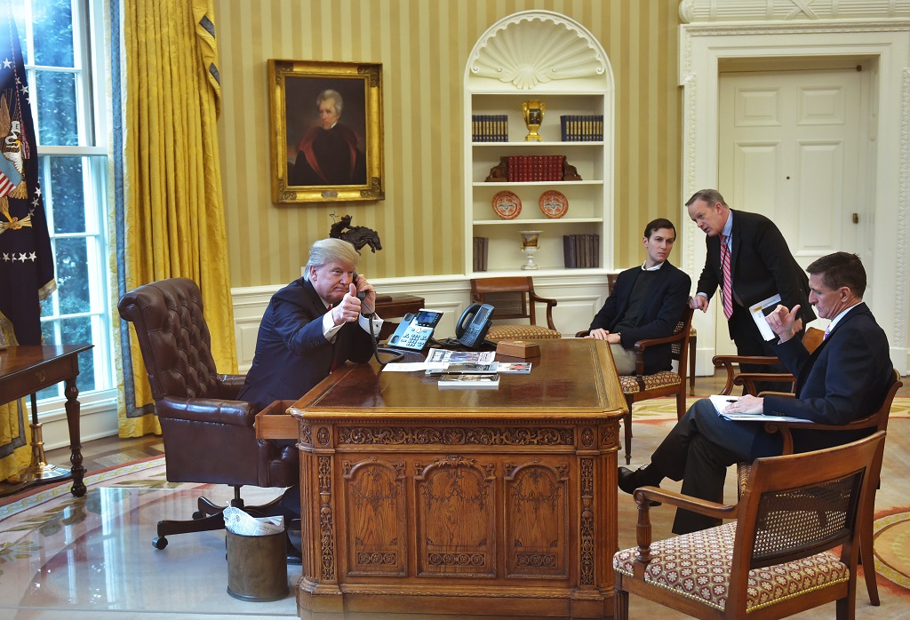 US President Donald Trump(L)seen through an Oval Office window gives a thumbs up as he speaks on the phone to King Salman of Saudi Arabia in the Oval Office of the White House on January 29, 2017 in Washington, DC. President Trump is speaking by phone with the leaders of Saudi Arabia and the United Arab Emirates, amid an uproar over his travel ban for some Muslim majority countries. / AFP PHOTO / MANDEL NGAN