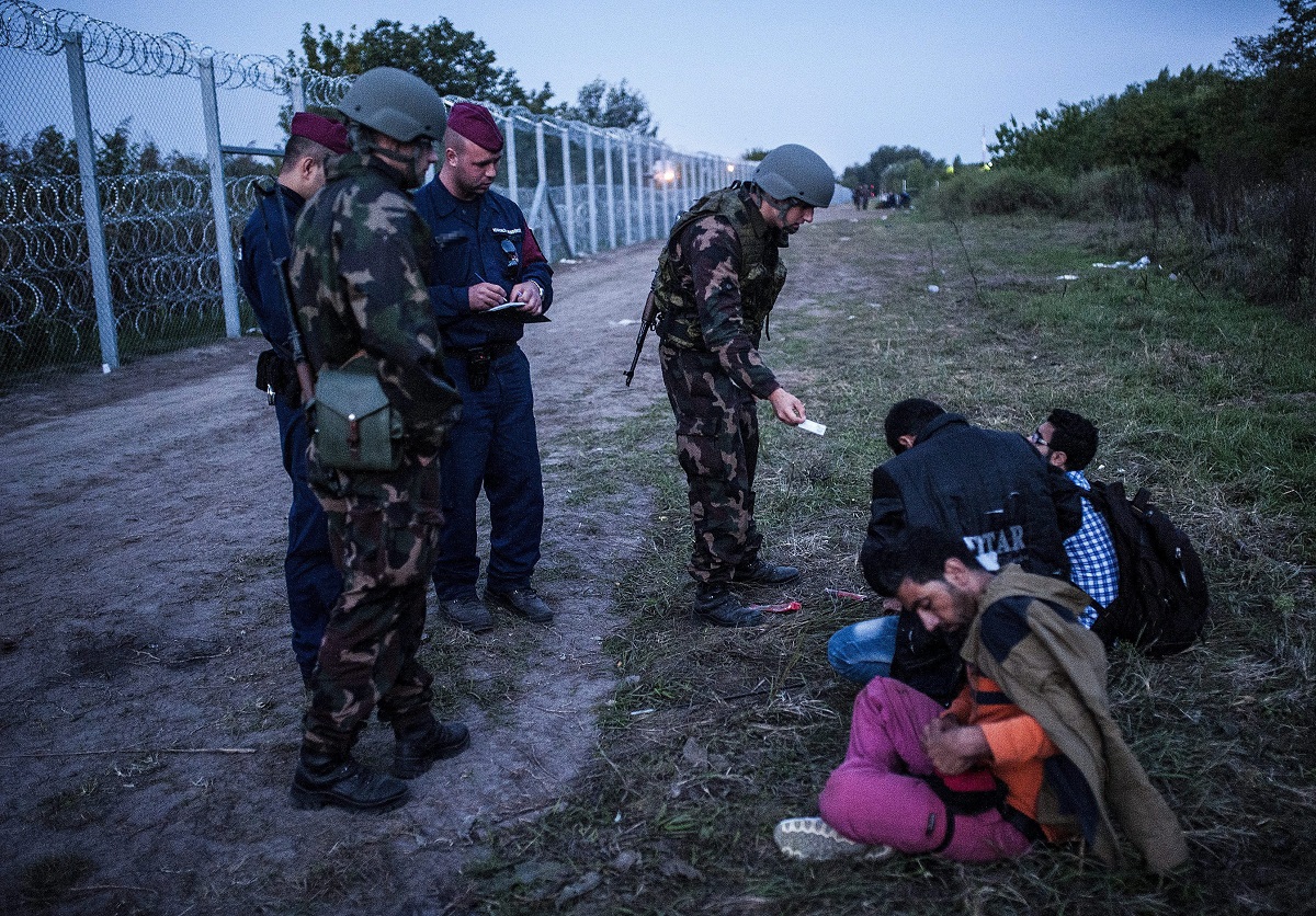 Katonák és rendőrök három elfogott illegális bevándorlót őriznek a biztonsági határzár mellett a szerb-magyar határon, Röszke térségében 2015. szeptember 15-én. MTI / Ujvári Sándor