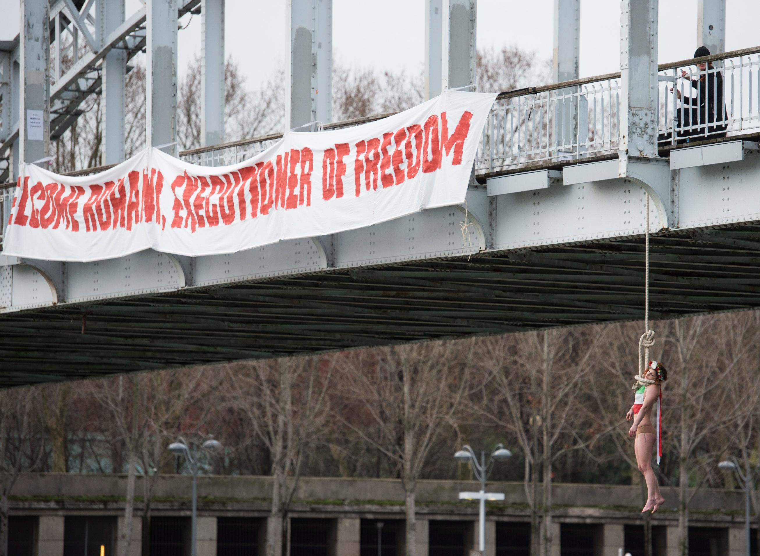 Párizs, 2016. január 28. Kötélen lóg egy hídról Sarah Constantin, a Femen nõjogi szervezet egyik aktivistája a Haszan Róháni iráni elnök kétéves elnöksége alatt elkövetett kivégzések elleni tiltakozásként Párizsban 2016. január 28-án, Róháninak a francia fõvárosban tett látogatásával egy idõben. A hídon látható transzparens jelentése: Isten hozott Róháni, a szabadság hóhéra!. (MTI/AP/Zacharie Scheurer)