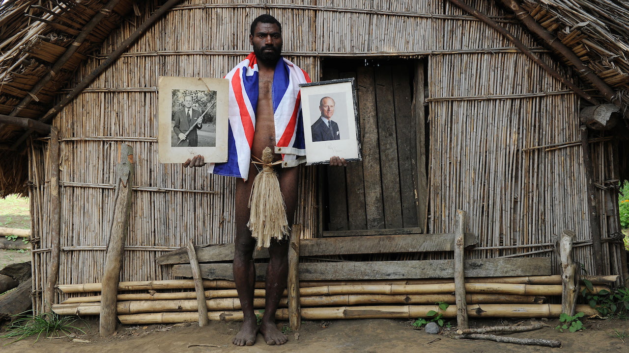 TO GO WITH AFP STORY "Vanuatu-Britain-religion-royals,FEATURE" by Madeleine Coorey Sikor Natuan, the son of the local chief, holds two official portraits (one holding a pig-killing club, L) of Britain's Prince Philip in front of the chief's hut in the remote village of Yaohnanen on Tanna in Vanuatu on August 6, 2010. In his remote village in Vanuatu, tribesman Sikor Natuan cradles a faded portrait of Britain's Prince Philip against his naked and tattooed chest. Natuan, who just weeks before danced and feasted to mark the royal's 89th birthday, is already preparing for next year's celebrations -- and he is expecting the guest of honour to attend, despite his advanced age. For in the South Pacific village of Yaohnanen on Vanuatu's Tanna island, where men wear nothing but grass penis sheaths, and marijuana and tobacco grow wild, Prince Philip is worshipped as a god. AFP PHOTO / Torsten BLACKWOOD / AFP / TORSTEN BLACKWOOD