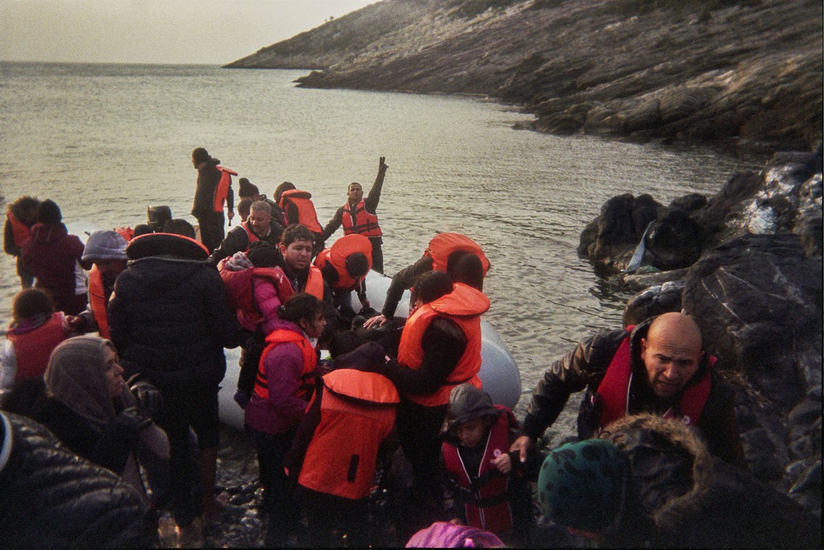 Refugees help each other to get off the dinghy. There have been no volunteers to help.