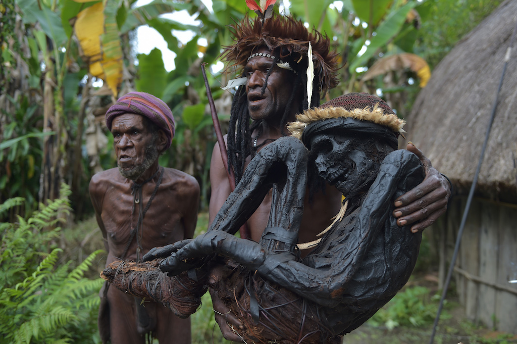 This photo taken on August 7, 2016 shows tribe chief Eli Mabel (C) holding the mummified remains of his ancestor, Agat Mamete Mabel, in the village of Wogi in Wamena, the long-isolated home of the Dani tribe high in the Papuan central highlands. Despite smoked mummification being no longer practised for Dani tribes people, they still preserve a number of mummies, some a few hundred years old, as a symbol of their highest respects to their ancestors, which in recent years has attracted tourists from around the world. / AFP PHOTO / ADEK BERRY