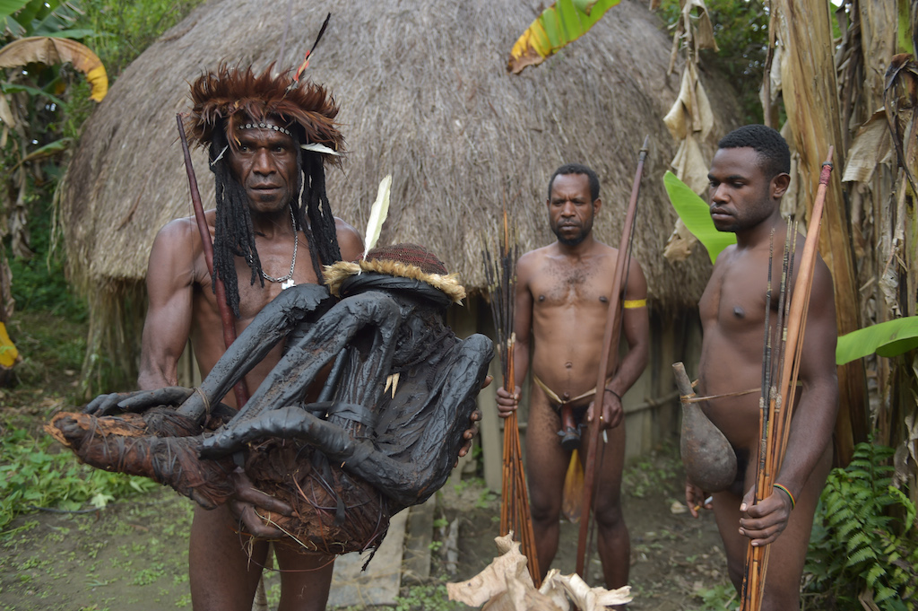 This photo taken on August 7, 2016 shows tribe chief Eli Mabel (L) holding the mummified remains of his ancestor, Agat Mamete Mabel, Agat Mamete Mabel, in the village of Wogi in Wamena, the long-isolated home of the Dani tribe high in the Papuan central highlands. Despite smoked mummification being no longer practised for Dani tribes people, they still preserve a number of mummies, some a few hundred years old, as a symbol of their highest respects to their ancestors, which in recent years has attracted tourists from around the world. / AFP PHOTO / ADEK BERRY