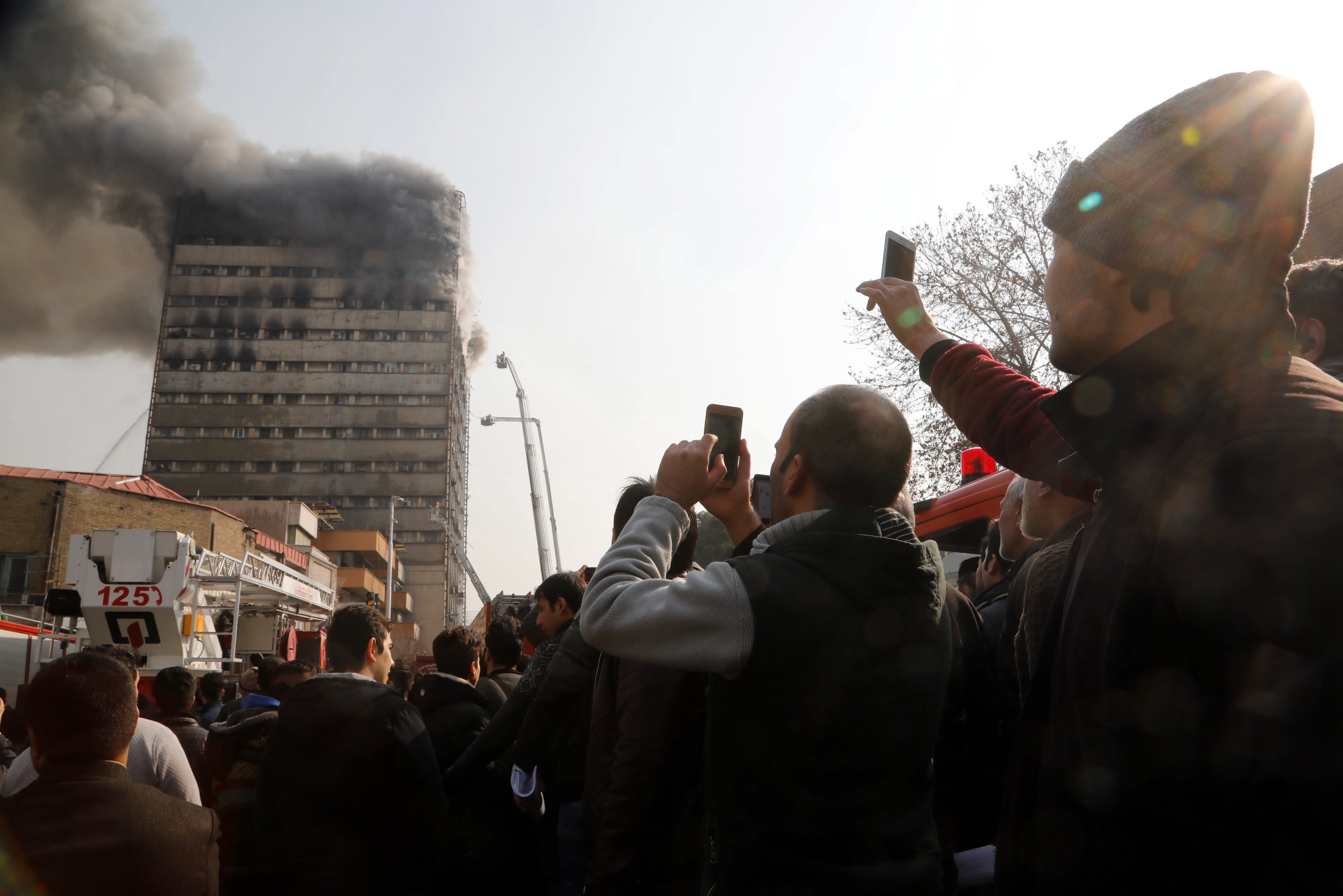 Teherán, 2017. január 19. A lángokban álló Plasco toronyház oltásáról készítenek felvételt járókelõk Teheránban 2017. január 19-én, miután egyelõre ismeretlen okból tûz ütött ki az épületben, amelynek felsõ szintjei beomlottak. Az iráni állami televízió szerint a felhõkarcolóban rekedt emberek és a tûzoltók közül többen életüket vesztették, legkevesebb 38-an megsérültek. (MTI/EPA/Abedin Taherkenareh)